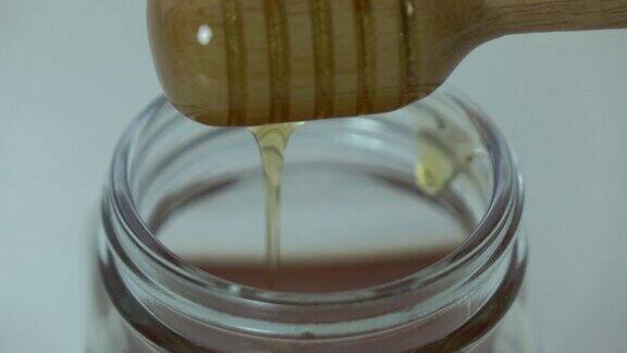 近距离蜂蜜流入一个玻璃罐使用蜂蜜勺