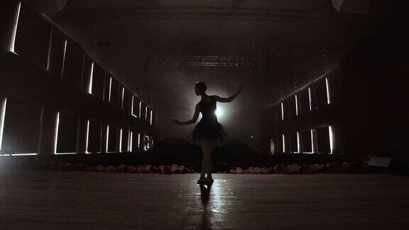 优雅的芭蕾舞者穿着黑色芭蕾舞裙在工作室与烟雾和背光