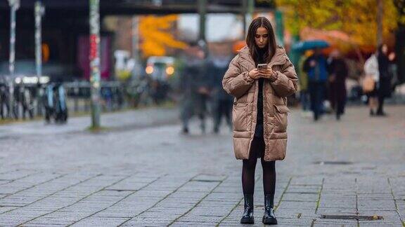 年轻女性在公共街道上用智能手机浏览社交媒体、查看新闻、玩手机游戏或发短信的时间流逝