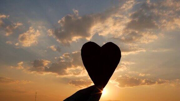 剪影的心形纸板在手和阳光透过心在日落的背景爱情和情人节