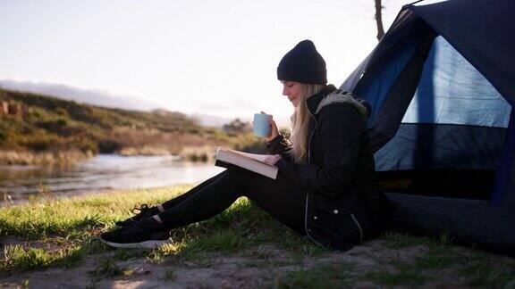 一段4k视频记录了一名年轻女子在一次露营旅行中坐着喝咖啡和阅读