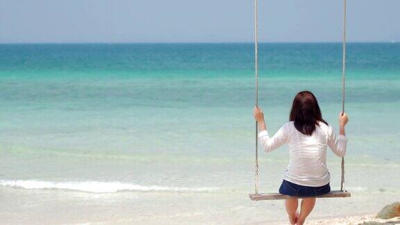女人在有大海和蓝天的沙滩上荡秋千放松概念4k(UHD)