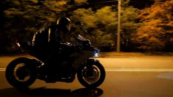 男人骑着现代黑色摩托车在夜晚的城市街道上飞驰一个骑摩托车的人在空旷的夜里与他的摩托车赛跑一个开着车灯的家伙自由侧视图