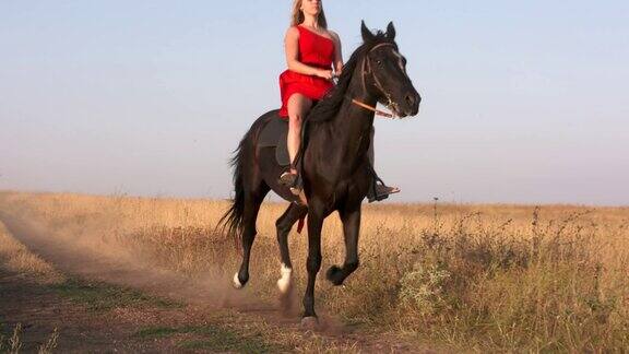穿着红色长裙的年轻女孩骑着黑马走过干燥的草原