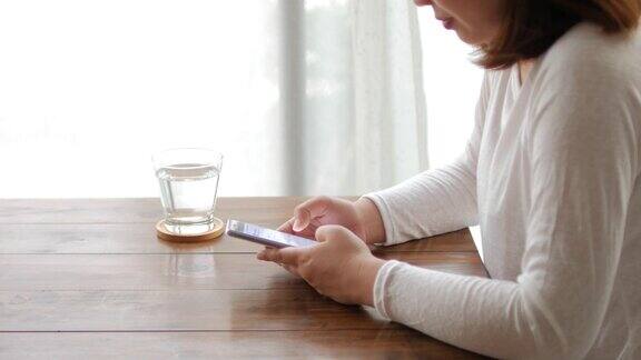女人在木桌上使用和触摸智能手机在家放松时间摄影车从右向左拍摄