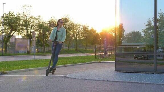 特写:日出时一名女子骑着她的电动滑板车绕着一座现代摩天大楼