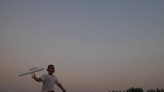 男孩玩着木头飞机在夕阳下奔跑在田野上