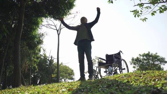 亚洲老人从户外公园的轮椅上站起来