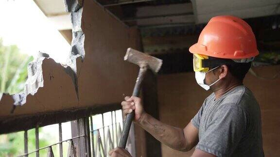 建筑工人戴着防护面具用大锤拆墙