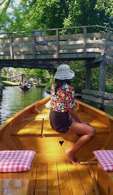 在荷兰基索恩运河的木船上戴着帽子的亚洲妇女荷兰基索恩:可以看到著名的基索恩村庄那里有运河和质朴的茅草屋顶房屋