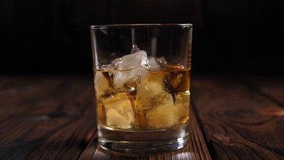 一杯在黑暗中木制背景上加冰的威士忌