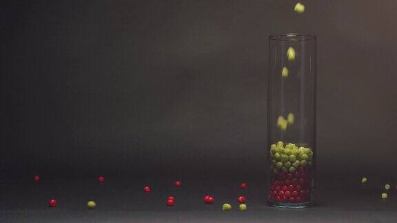 用慢镜头拍摄蓝色糖果落在粉红、红色和绿色的玻璃花瓶上复制空间是黑色的黑板纹理背景