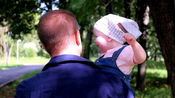 年轻的爸爸抱着宝贝女儿在城市公园里一家人宝贝看着镜头