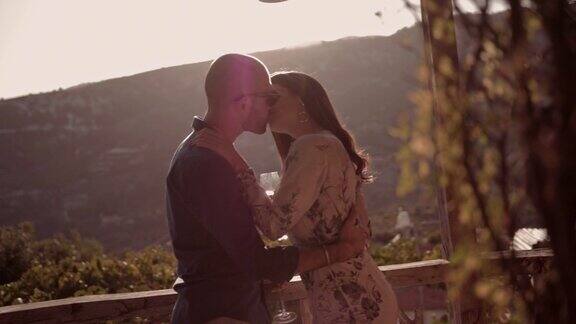 年轻的情侣亲吻和喝葡萄酒在葡萄园小屋阳台上