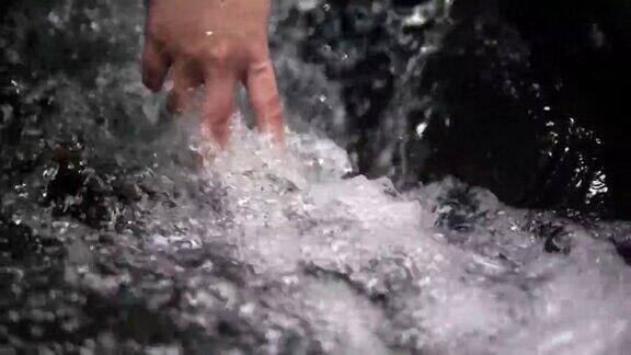 手触摸干净的水飞溅的溪流自然瀑布