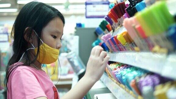 亚洲女孩戴着口罩在文具店选择笔与家人社会距离的生活理念
