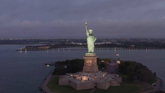 美丽的自由女神像在日出或黄昏与美国国旗挥舞的背景空中滑左多莉