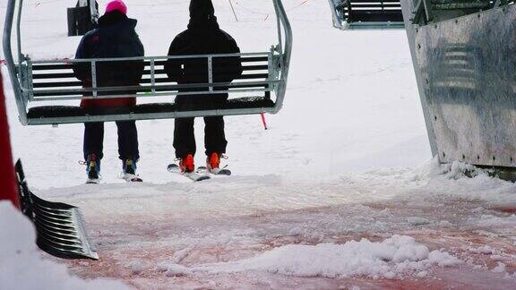 一个滑雪缆车举起两个滑雪者而有人铲雪从滑板平台在一个滑雪场在冬天