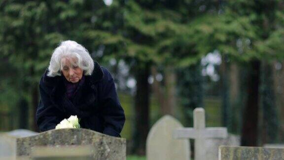 悲伤的老妇人拿着鲜花站在墓前