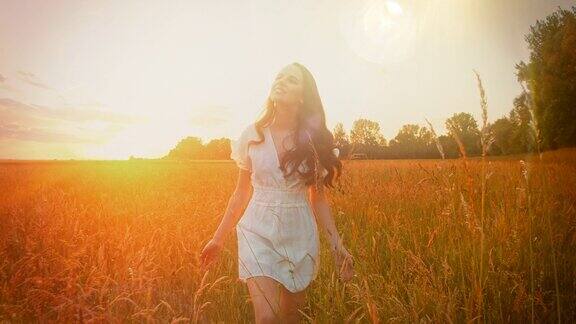 一个穿着白色裙子的女人在日落时走在草地上