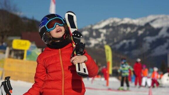 滑雪胜地的男孩一个穿着全套滑雪装备的孩子穿着红色夹克戴着眼镜和头盔望着天空阳光灿烂