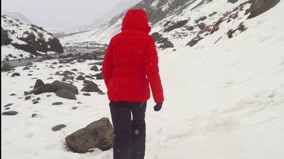 后视图的年轻女子在红色夹克行走在冬天的山冰岛的雪山