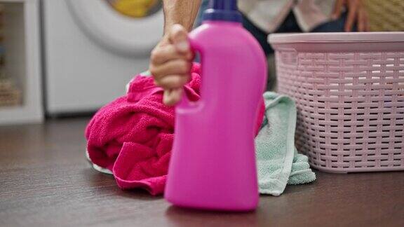 年轻的西班牙裔男子洗衣服把洗衣液瓶放在洗衣房的地板上