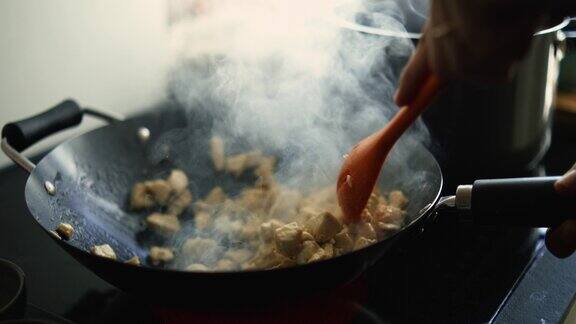 特写镜头:用手在厨房炉子的热锅上以800帧秒的慢速搅拌鸡肉有烟冒出来人正在准备饭菜