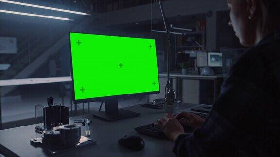 OvertheShoulderShot的工程师工作与绿色模拟屏幕桌面计算机在夜间的背景工程设施中展示工业设计蓝图和图纸
