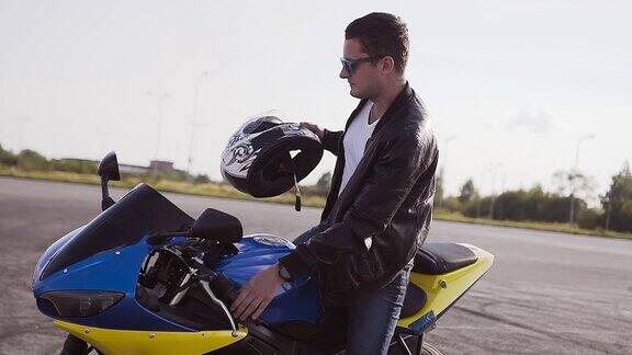 摩托车手穿着皮夹克和牛仔裤走向他的摩托车坐在他身上戴着太阳镜