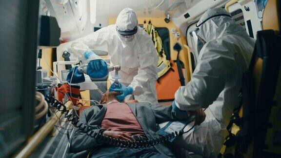 身穿一次性工作服的急救护理人员在送往医院的途中为受伤的病人提供医疗帮助急救助理在救护车上戴上无创通气面罩