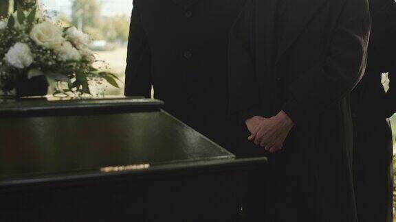 在户外葬礼上人们穿着黑色外套站在棺材旁