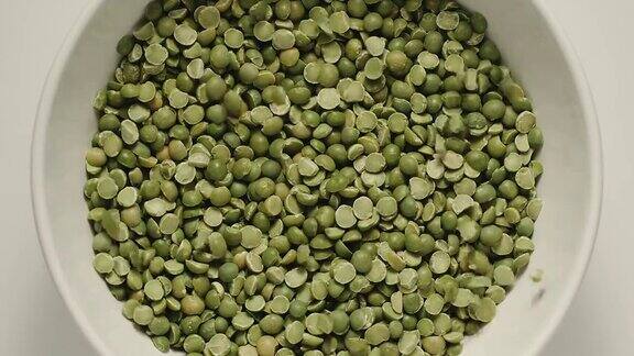 慢镜头:绿色的豌豆掉进一个白色的碗里-俯视图