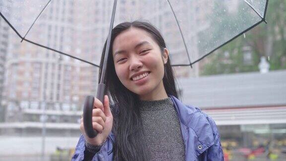 快乐的亚洲女人微笑着享受着雨撑着透明的伞走在城市里