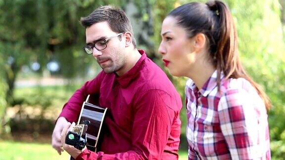 一对年轻夫妇在公园里弹吉他唱歌