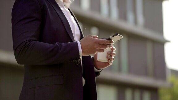 在街上拿着纸杯用智能手机的商人