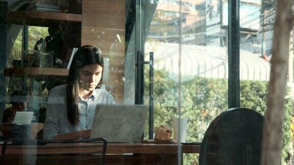 美丽的亚洲女性在咖啡馆用笔记本电脑工作日落时分