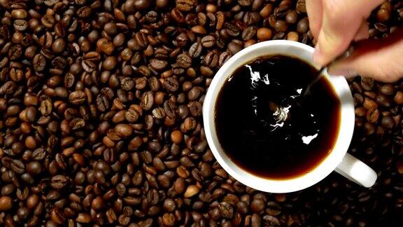 将咖啡倒入白色的杯子中搅拌然后用手挑出一个放在烘培咖啡豆堆上的杯子