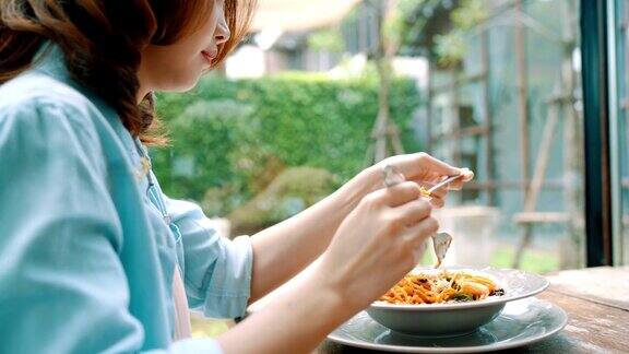 美丽快乐的亚洲女人吃一盘意大利海鲜意大利面在餐厅或咖啡馆同时微笑和看食物