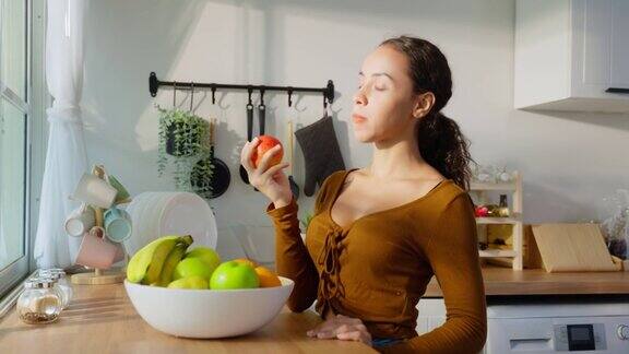 年轻迷人的拉丁裔女子在家里厨房的餐桌上吃水果美丽活跃的女性喜笑颜开地站着享受吃香蕉保健健康减肥的健康食品