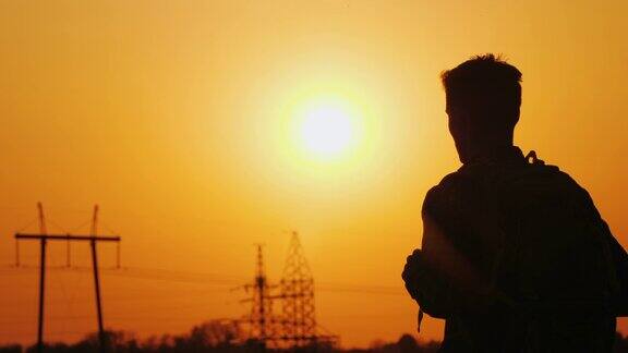 一个背着背包的男子站在远处的城市风景和夕阳的背景下