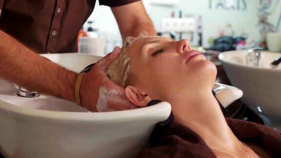 男发型师在现代美容院给一个金发女人洗头