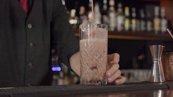 调酒师将桃色鸡尾酒从摇酒器倒入盛满冰块的玻璃杯中