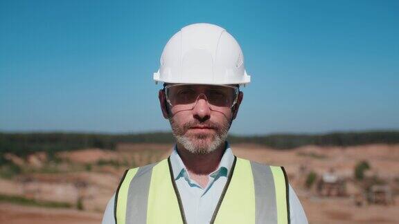 英俊的采石场工人的肖像戴着安全制服的护目镜和安全帽中年男性大胡子工程师看着镜头在温暖阳光明媚的日子里专业的采砂项目