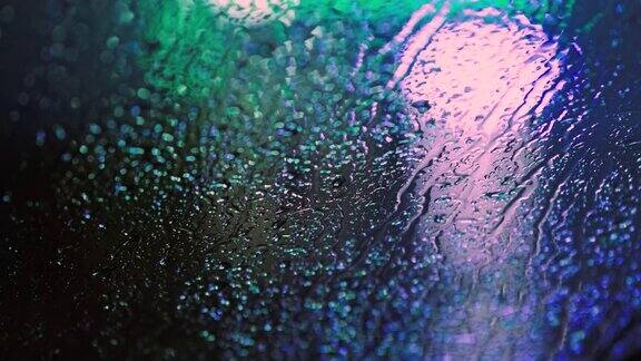 在夜晚雨水滴在车窗玻璃上与模糊的交通灯背景