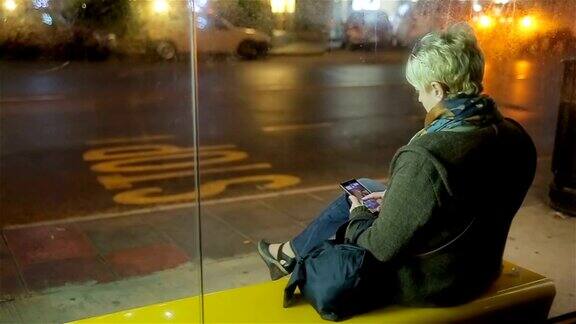 中年妇女在车站等车并使用手机夜景