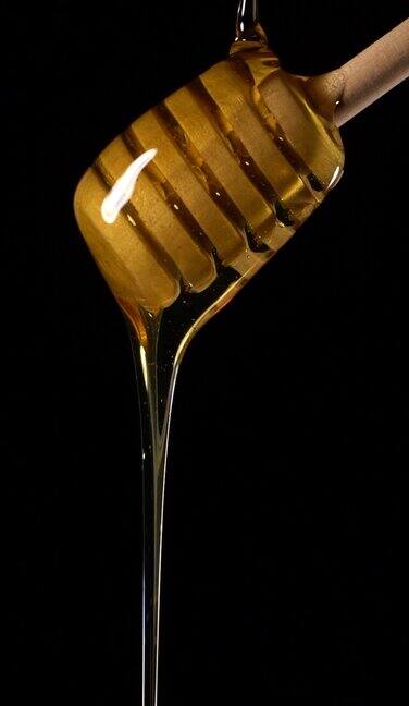 (慢动作和垂直)蜂蜜从一个木制的蜂蜜勺流出