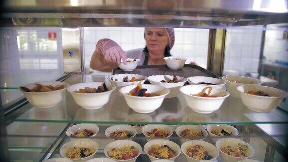 自助餐厅自助餐厅在自助餐厅或慈善社区汤厨房的陈列柜里女服务员把沙拉放在小碗里