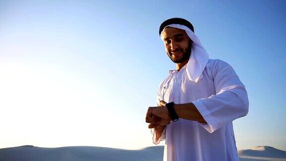 英俊的阿拉伯商人的肖像谁体验新的智能手表和站在广阔的沙漠中炎热的太阳在白天