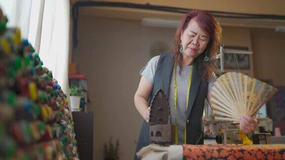 一名亚洲华裔高级女性裁缝在她的工作室里给古董铁器具扇风在熨布之前先加热